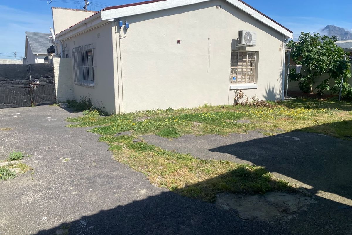Rear exterior view of the property featuring an asphalt driveway, security bars on windows, and an external air conditioning unit.