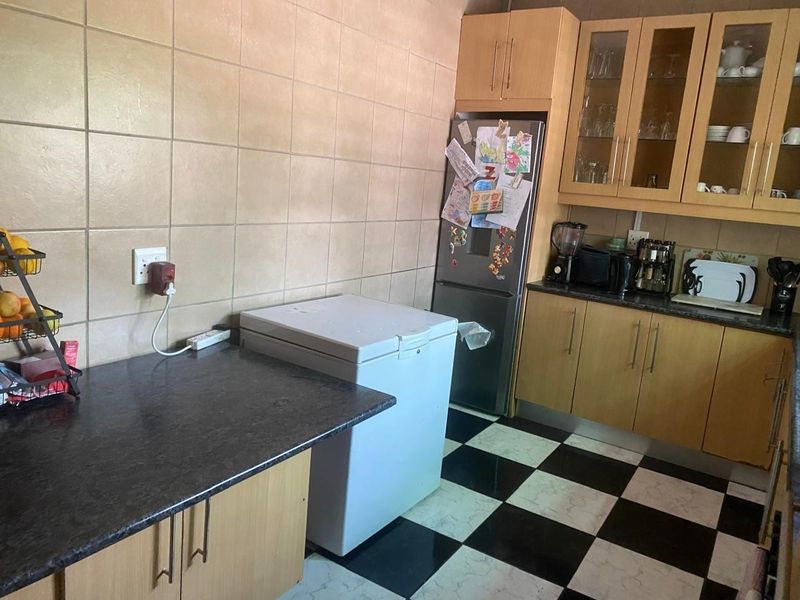A functional kitchen featuring light wood cabinetry, dark laminate countertops, tiled splashbacks, and a distinctive black and white checkered floor.