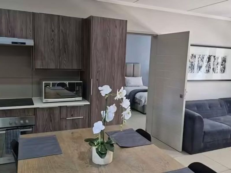 Open-plan living area featuring a modern kitchen with wood-grain cabinetry, integrated appliances, and tiled flooring, leading into an adjacent bedroom.