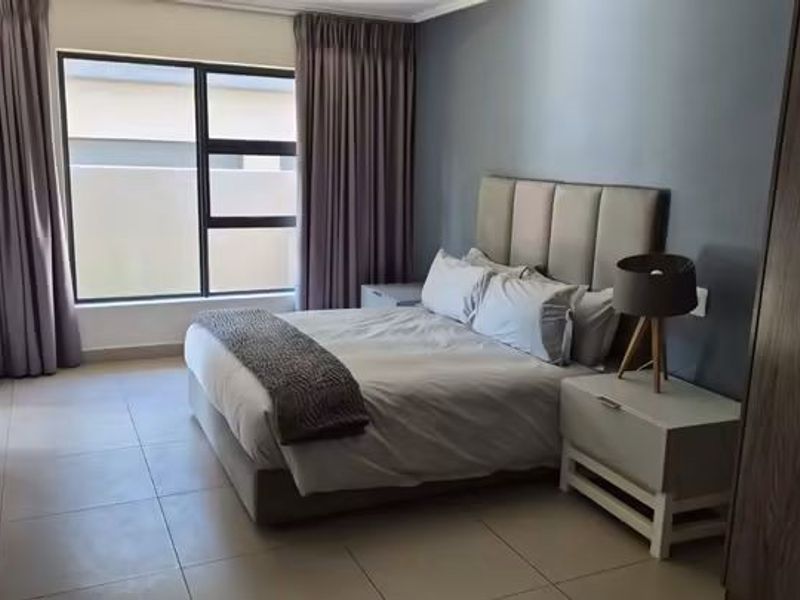A well-maintained bedroom featuring neutral tiled flooring, large aluminium-framed windows, and an integrated air conditioning unit.