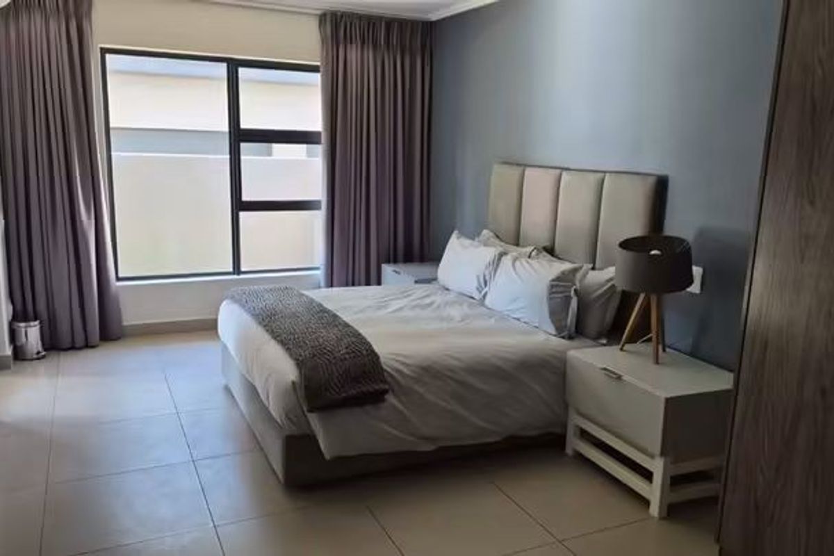 A well-maintained bedroom featuring neutral tiled flooring, large aluminium-framed windows, and an integrated air conditioning unit.