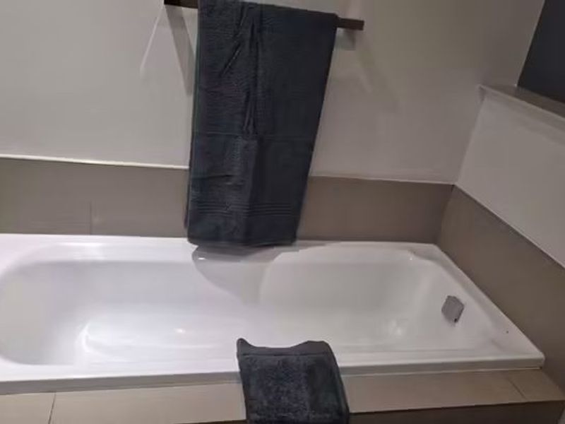 A clean, modern bathroom featuring a built-in bathtub with neutral-toned tiled surround and a wall-mounted towel rail.