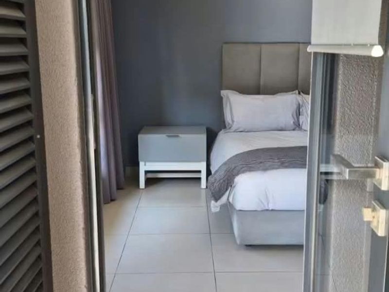A view into a modern bedroom featuring neutral grey tones, tiled flooring, and direct access through a sliding glass door.