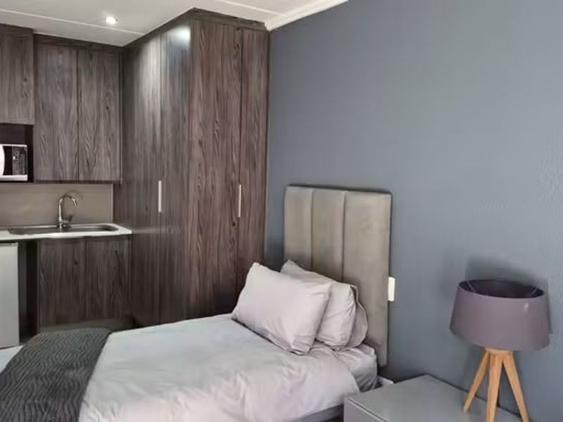 A bedroom featuring built-in cupboards and a compact kitchenette with a sink and built-in microwave.