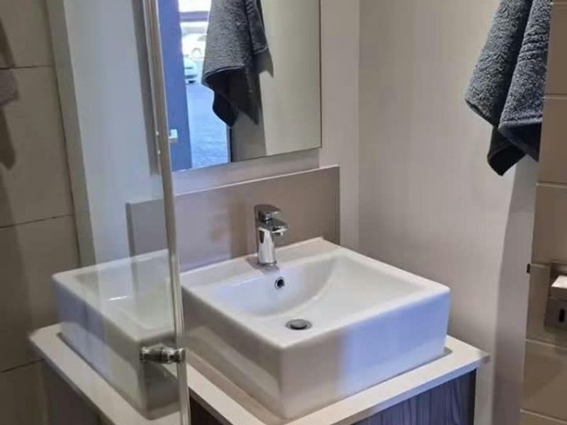 Modern bathroom featuring a vessel sink with a vanity cabinet, chrome mixer tap, and a glass shower screen.