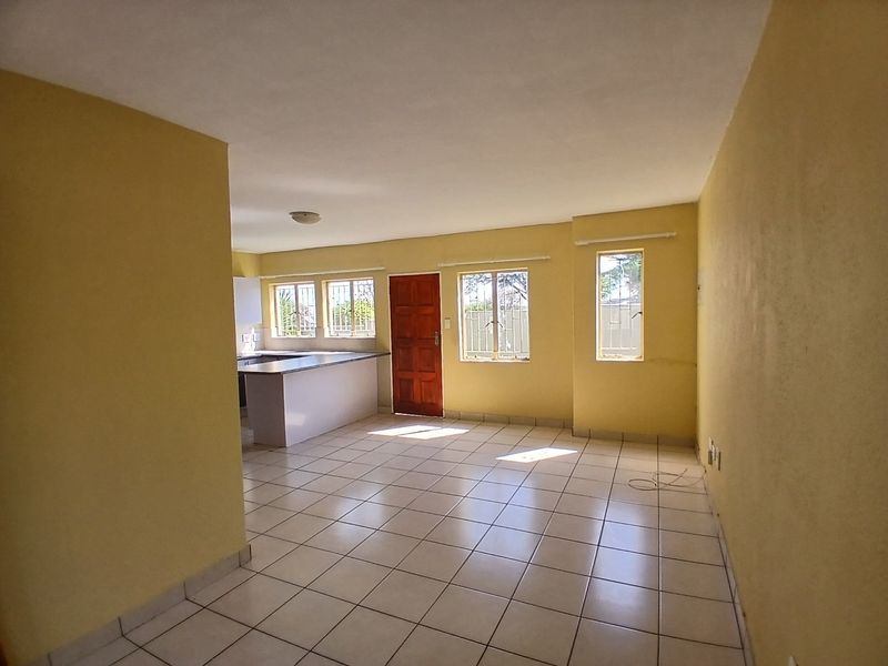 Spacious open-plan living area featuring tiled flooring, security-barred windows, and an integrated kitchen counter, offering a blank canvas for interior design.