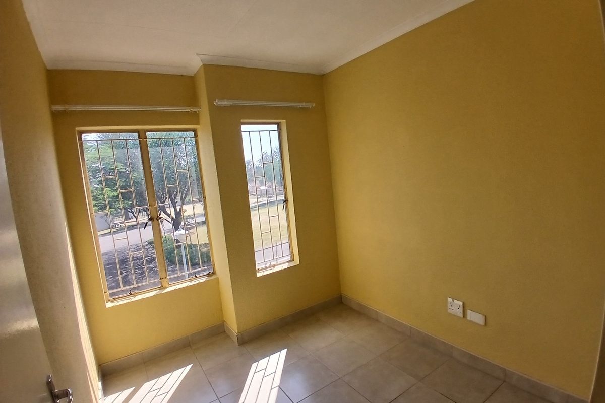 An empty bedroom featuring tiled flooring, yellow painted walls, and windows fitted with security bars.