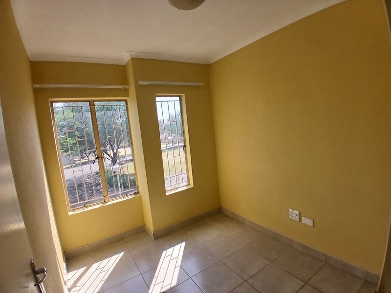 An empty bedroom featuring tiled flooring, yellow painted walls, and windows fitted with security bars.