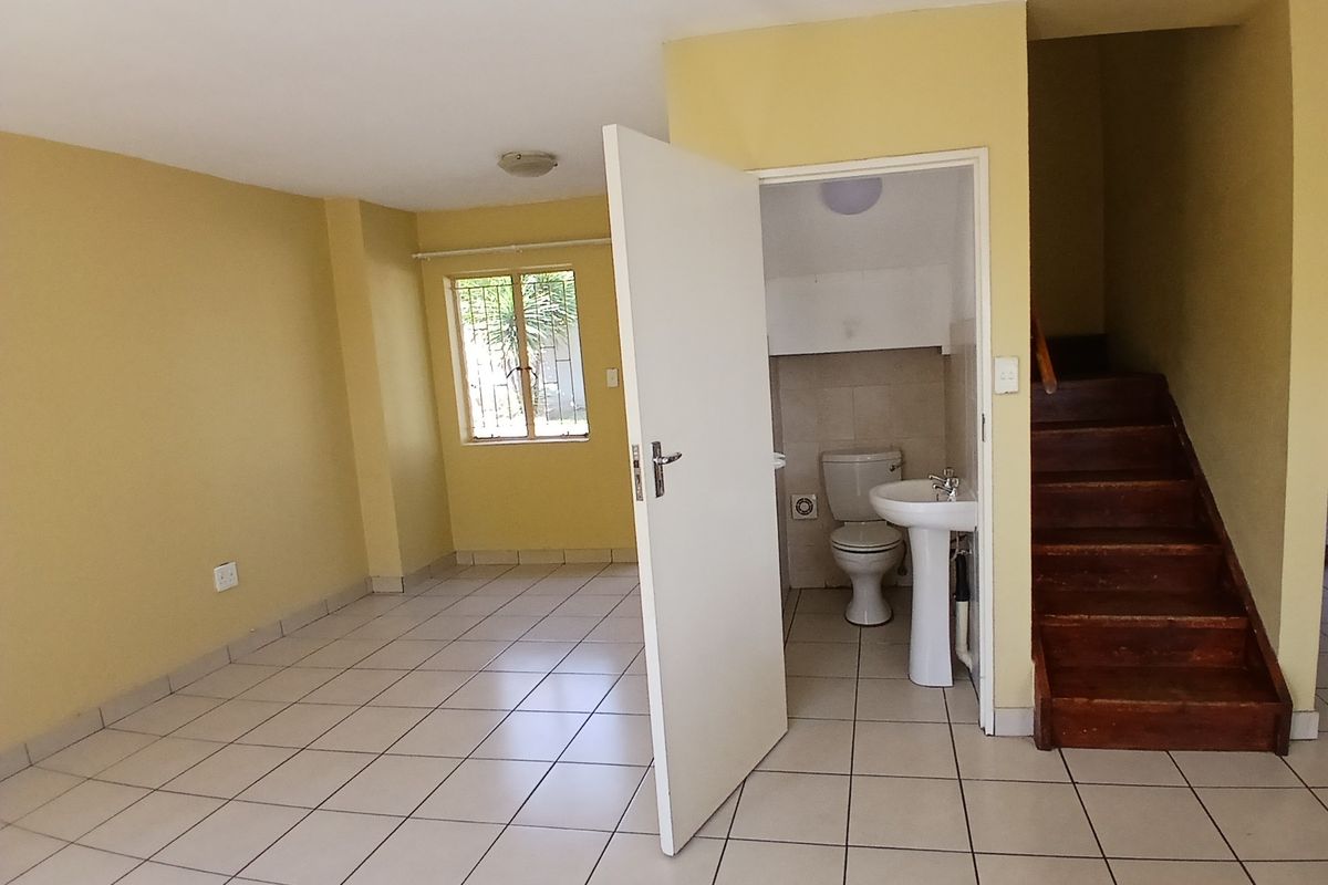 An open-plan living area featuring tiled flooring, a wooden staircase, and an adjacent guest bathroom with a pedestal basin and toilet.