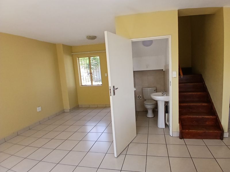 An open-plan living area featuring tiled flooring, a wooden staircase, and an adjacent guest bathroom with a pedestal basin and toilet.