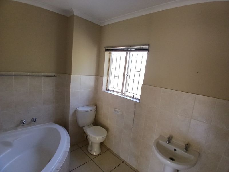 A functional bathroom featuring a built-in bathtub, pedestal basin, and toilet, finished with neutral wall and floor tiles.