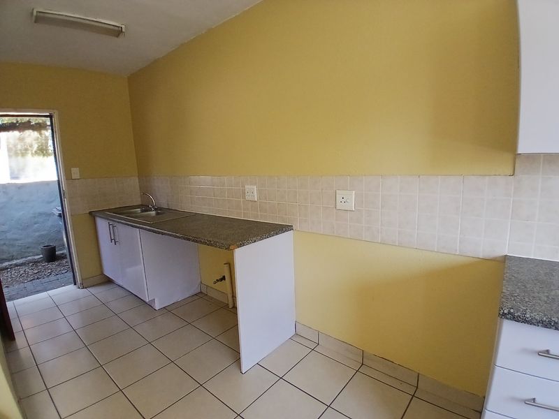 A functional kitchen area featuring built-in cabinetry, a stainless steel sink, tiled backsplash, and ceramic flooring, with direct access to an outdoor space.