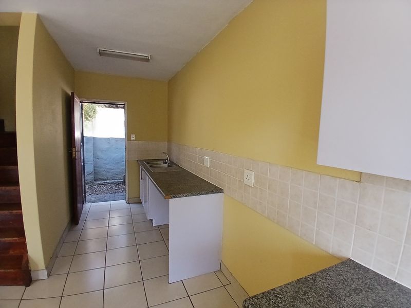 A functional kitchen area featuring built-in cabinetry, laminate countertops, and tiled flooring, with direct access to an outdoor space.