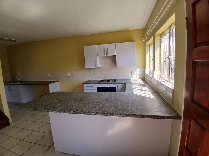 A functional, empty kitchen featuring built-in cabinetry, laminate countertops, a gas hob, and an integrated oven, with tiled flooring and natural light.