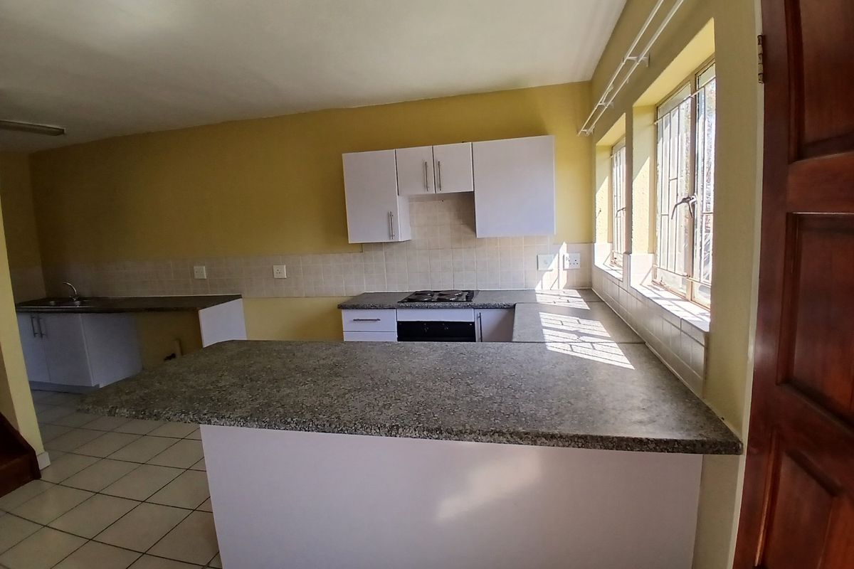 A functional, empty kitchen featuring built-in cabinetry, laminate countertops, a gas hob, and an integrated oven, with tiled flooring and natural light.
