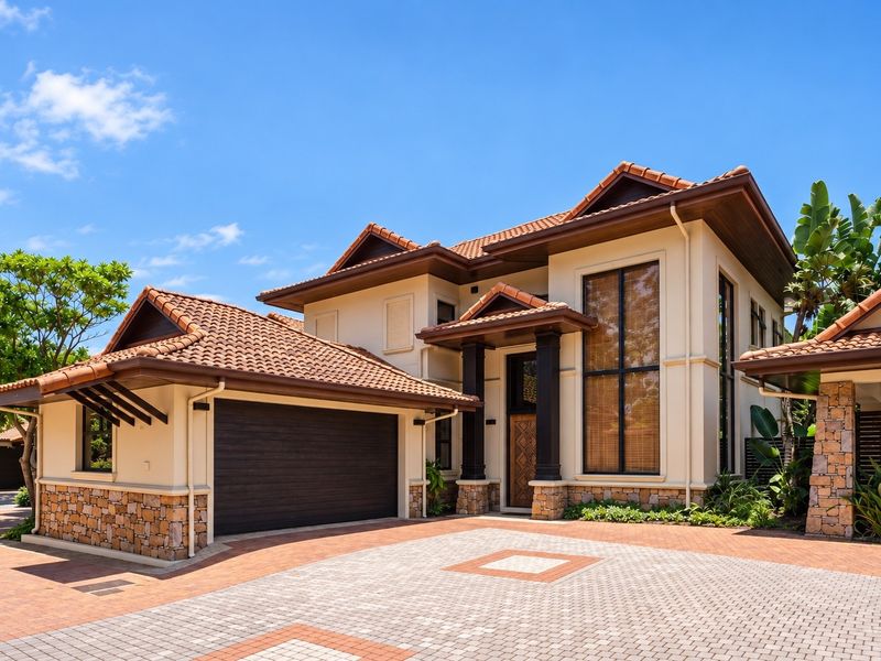 A well-maintained townhouse exterior featuring terracotta roof tiles, stone cladding accents, a double garage, and a paved driveway entrance.