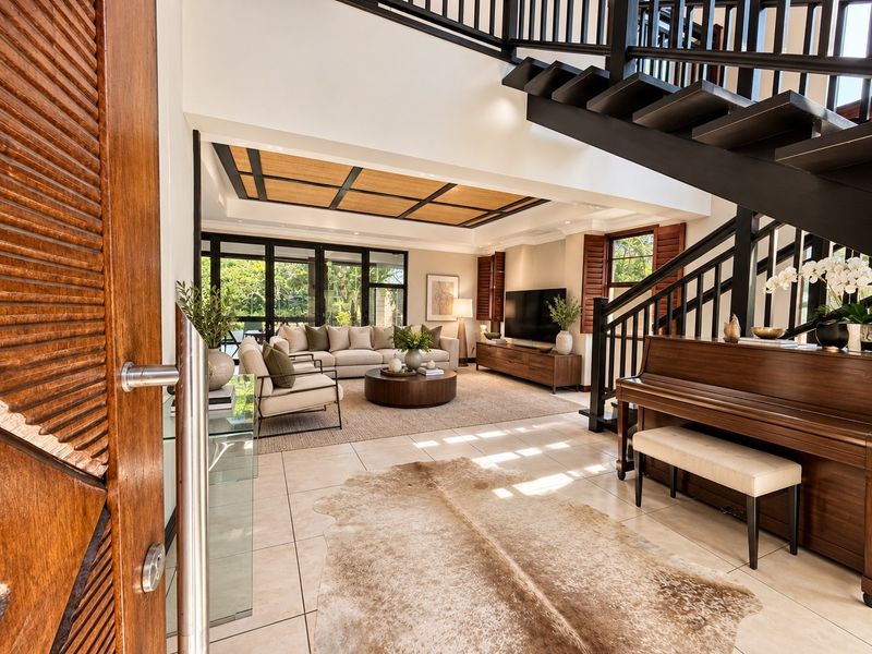 Spacious open-plan living area featuring a grand staircase, tiled flooring, coffered ceiling, and large sliding glass doors leading to the outdoor space.