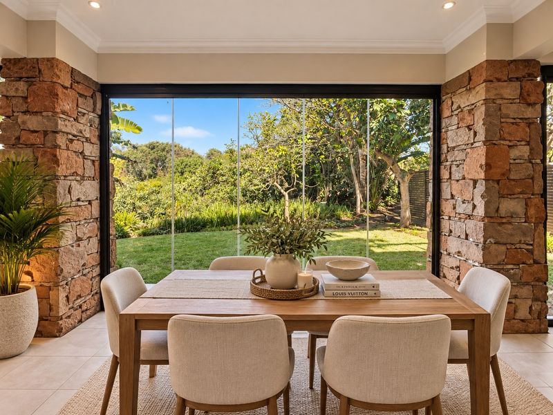 Elegant dining area featuring striking stone-clad pillars and expansive frameless glass doors that provide seamless indoor-outdoor flow to the lush garden.
