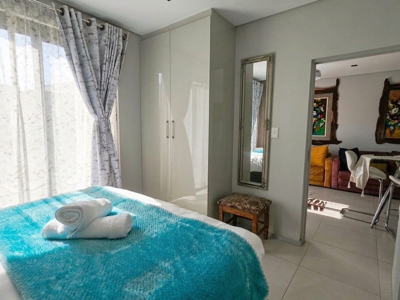 A bright bedroom featuring built-in wardrobes, tiled flooring, and a sliding glass door providing natural light, with an adjacent view into the living area.