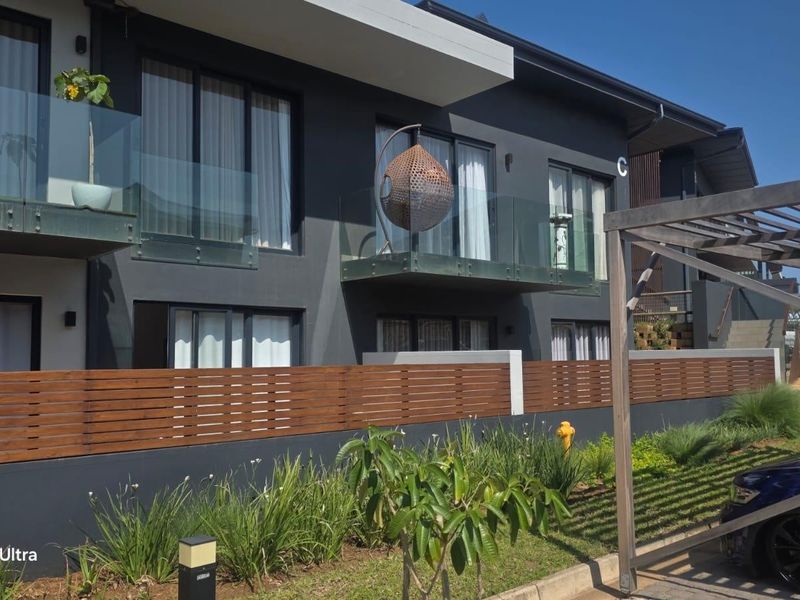 Modern apartment exterior featuring dark facade, glass balustrades, and timber slat fencing with a well-maintained garden area.