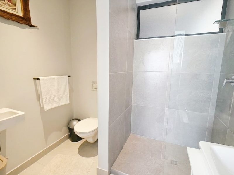 A modern bathroom featuring a walk-in shower with glass screen, wall-mounted basin, and toilet, finished with neutral wall tiles.