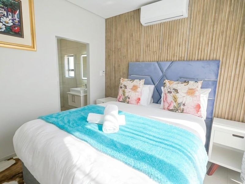 A well-maintained bedroom featuring a modern timber slat accent wall, integrated air conditioning, and direct access to an en-suite bathroom.