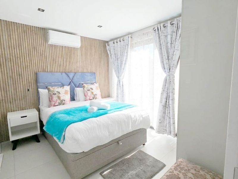 A modern, well-maintained bedroom featuring stylish slatted timber wall paneling, recessed lighting, and a wall-mounted air conditioning unit.