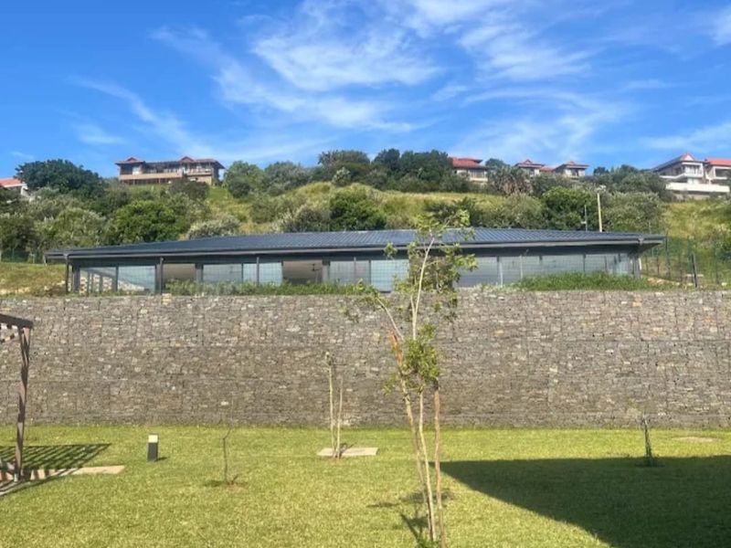 Rear view of the property featuring a large stone retaining wall, expansive glass sliding doors, and a well-maintained lawn area.