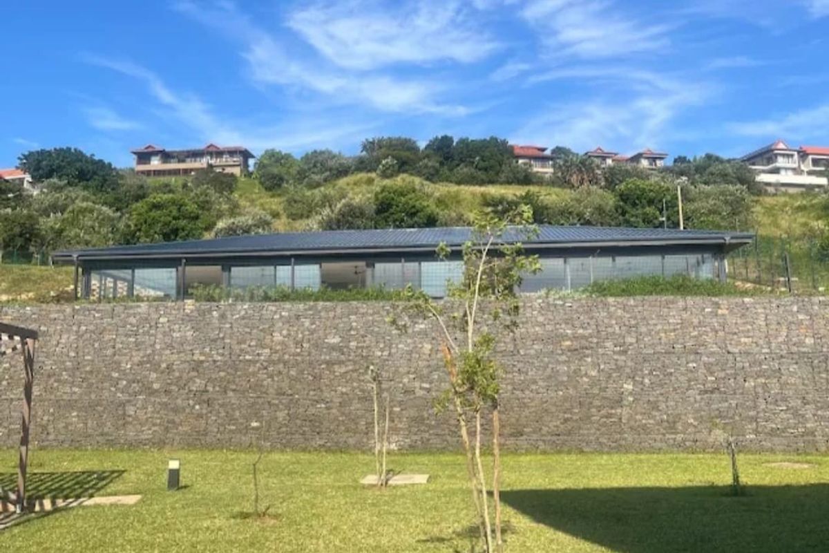 Rear view of the property featuring a large stone retaining wall, expansive glass sliding doors, and a well-maintained lawn area.