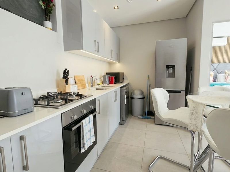 Modern kitchen featuring sleek high-gloss cabinetry, integrated gas hob, electric oven, and tiled flooring, offering a clean and functional culinary space.
