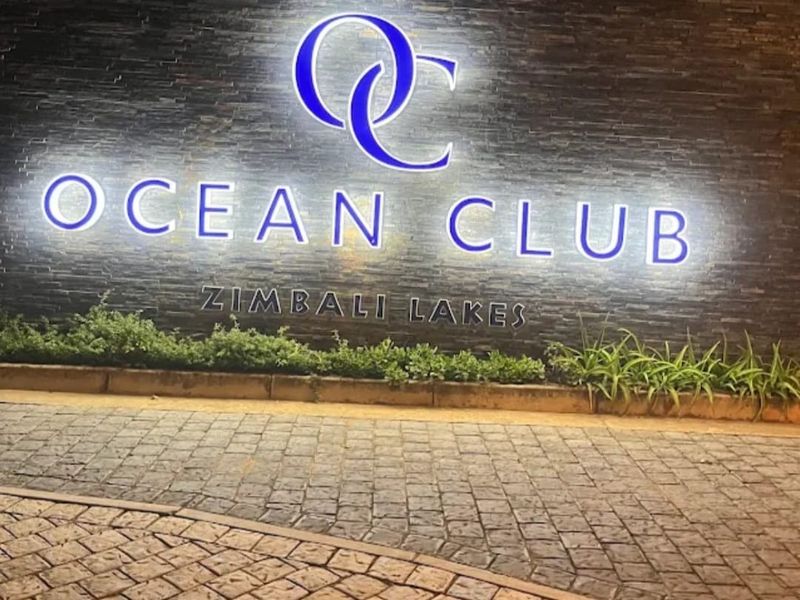 The entrance signage for Ocean Club at Zimbali Lakes, featuring illuminated branding on a stone-clad feature wall and a cobblestone driveway.