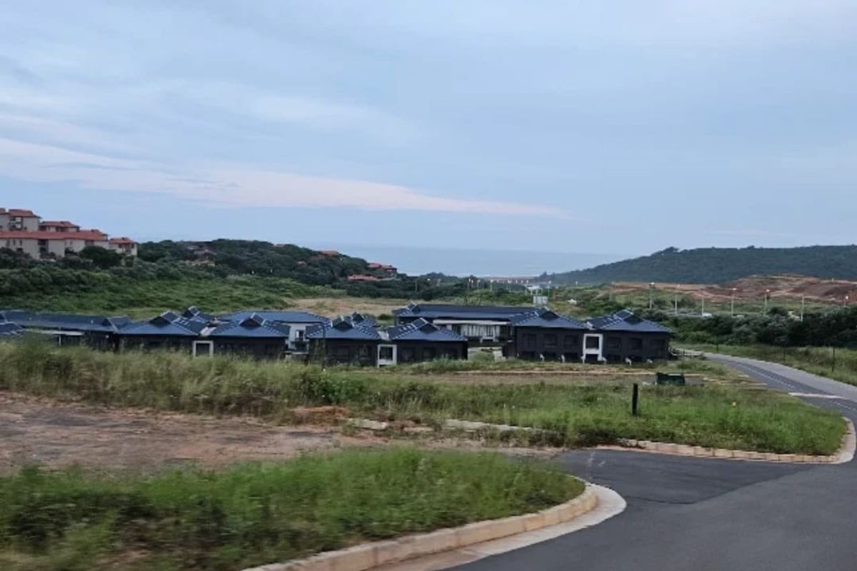 An elevated view of a residential development complex featuring multiple units with dark pitched roofs, surrounded by natural landscape and access roads.