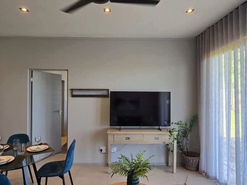 A bright and modern living area featuring tiled floors, recessed downlights, a ceiling fan, and large windows dressed with elegant sheer curtains.