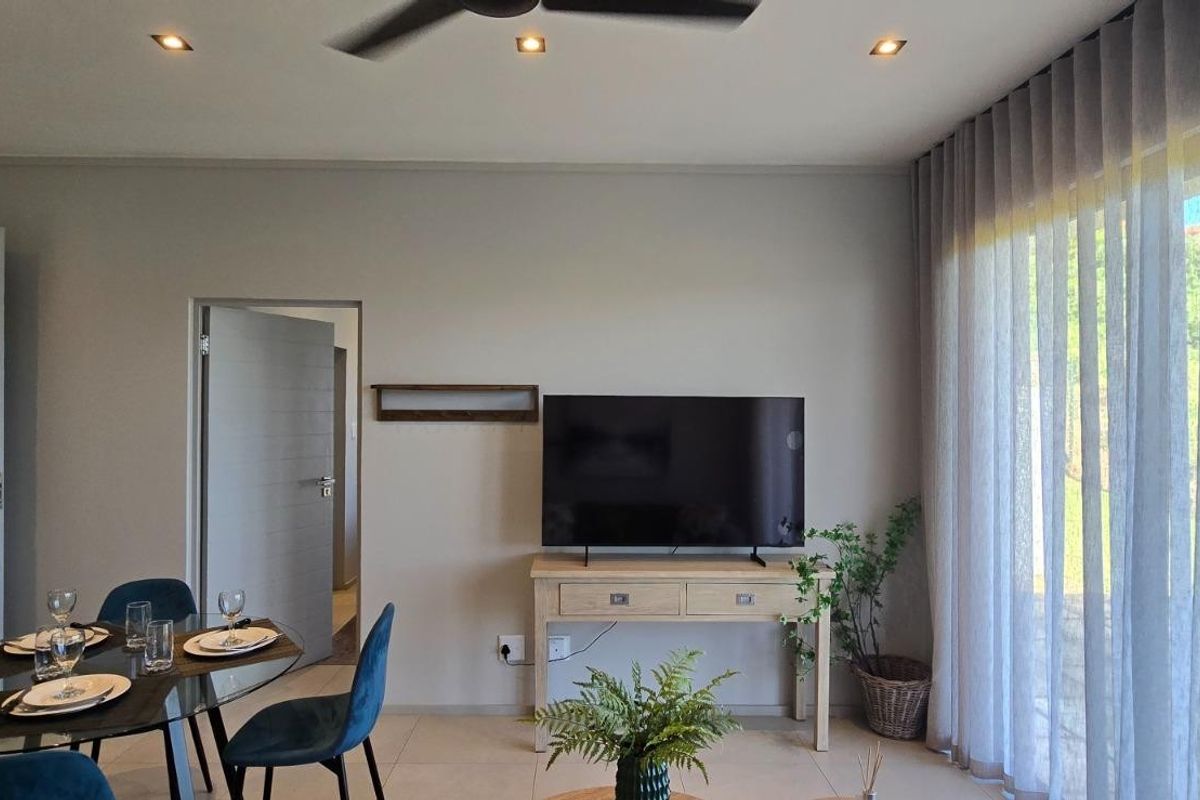 A bright and modern living area featuring tiled floors, recessed downlights, a ceiling fan, and large windows dressed with elegant sheer curtains.