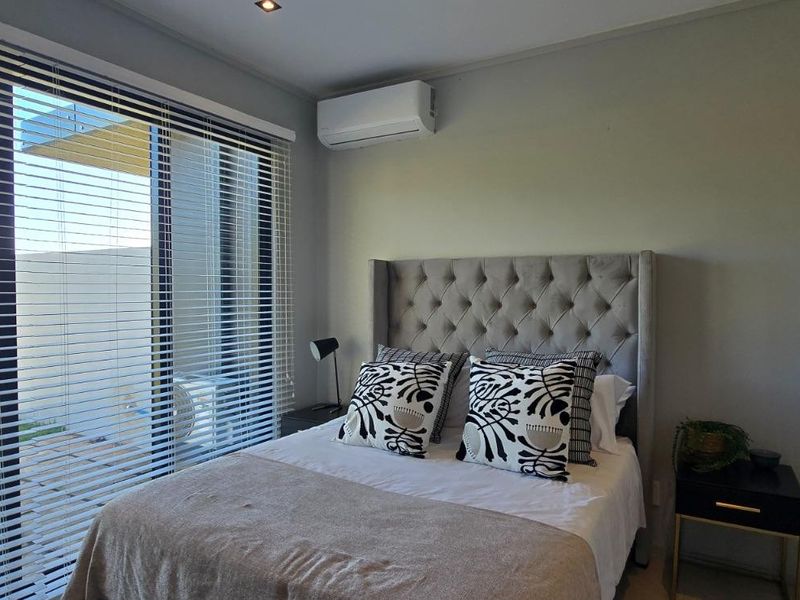 A modern bedroom featuring a split-system air conditioner, recessed lighting, and large sliding glass doors with venetian blinds providing access to the outdoors.