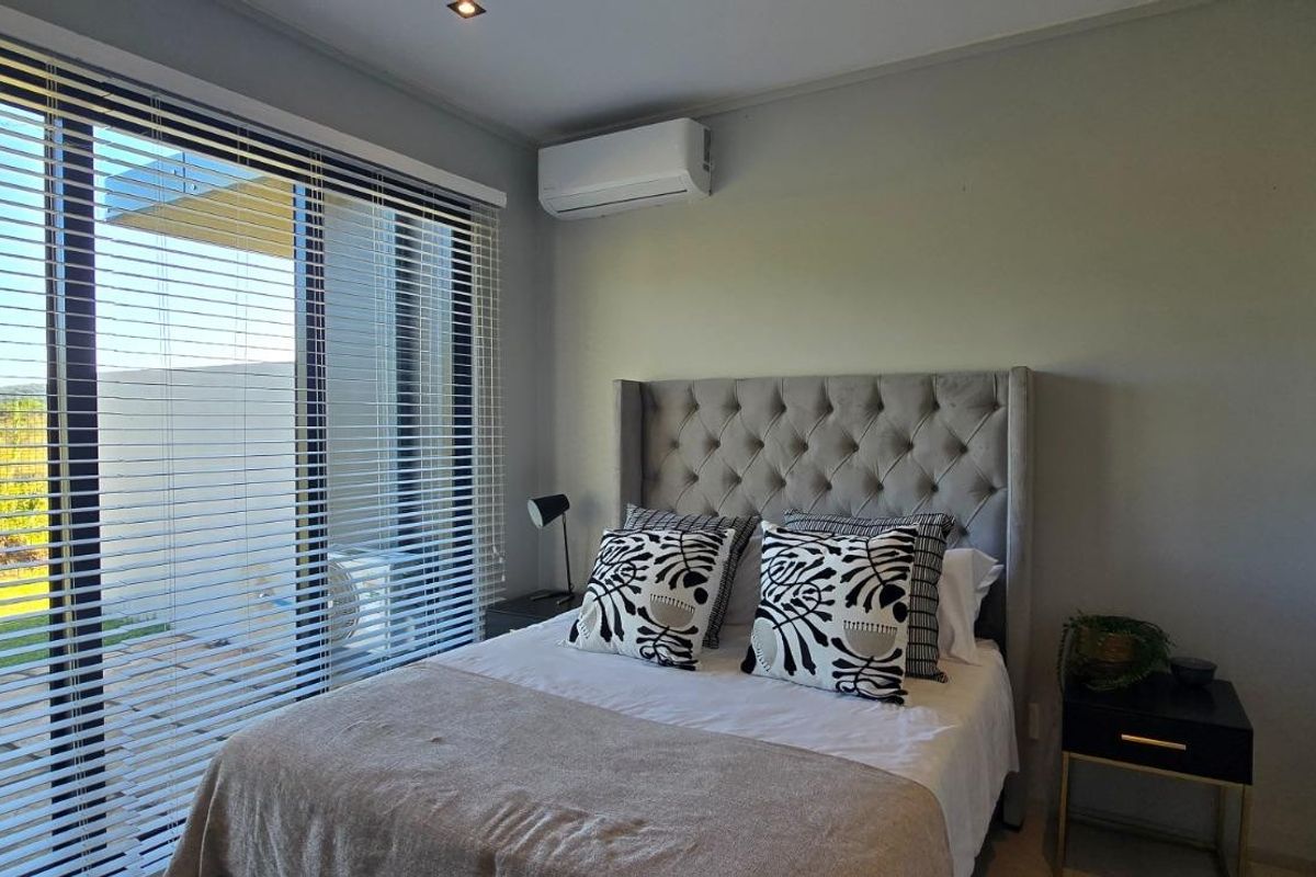 A modern bedroom featuring a split-system air conditioner, recessed lighting, and large sliding glass doors with venetian blinds providing access to the outdoors.