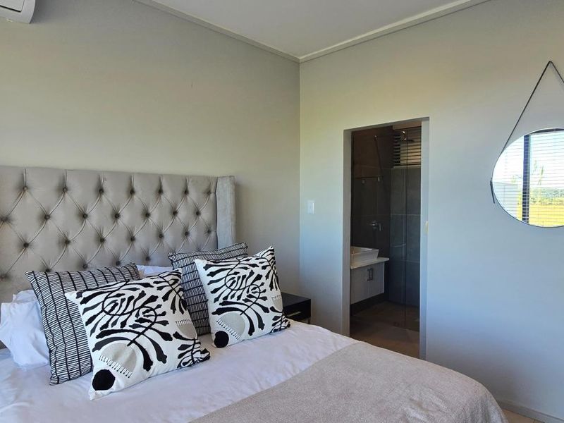 A well-maintained bedroom featuring neutral wall tones, an integrated air conditioning unit, and direct access to an en-suite bathroom.