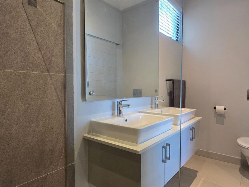 Modern bathroom featuring a double vanity with built-in cabinetry, a wall-mounted toilet, and a spacious glass-enclosed shower with tiled finishes.