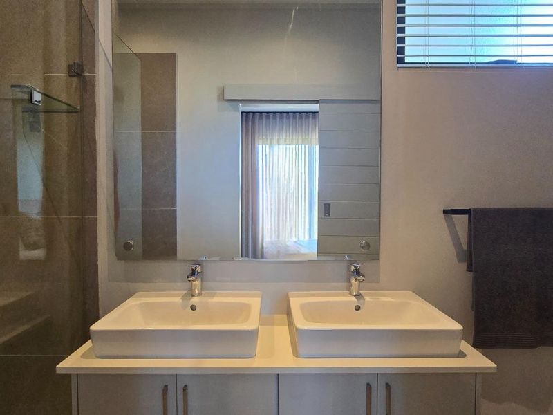 Modern bathroom featuring a double vanity with vessel sinks, a large wall-mounted mirror, and a glass-enclosed shower with neutral tiling.