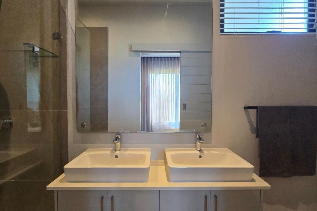 Modern bathroom featuring a double vanity with vessel sinks, a large wall-mounted mirror, and a glass-enclosed shower with neutral tiling.