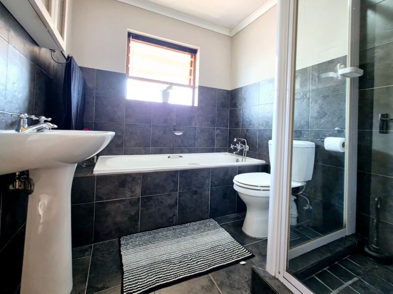 A modern bathroom featuring dark tiled walls, a pedestal basin, a built-in bathtub, and a separate shower enclosure.