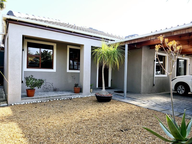 Front elevation of a well-maintained house featuring a paved driveway, covered patio area, and neat gravel landscaping.