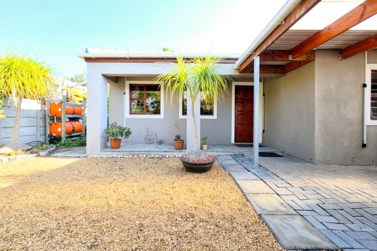 A well-maintained rear exterior featuring a paved walkway, gravel garden area, and a timber pergola providing shade over the entrance.