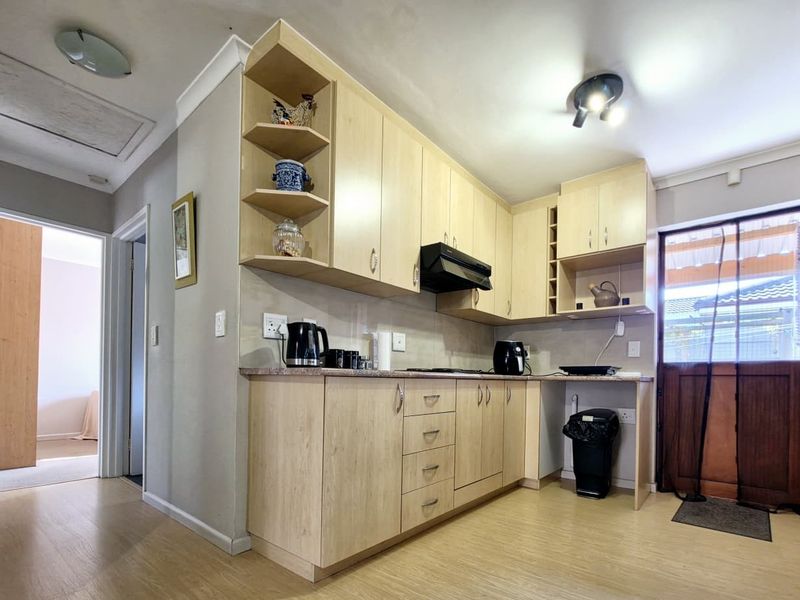 A functional kitchen featuring light wood-tone cabinetry, laminate countertops, and an integrated extractor fan, with direct access to an exterior door.