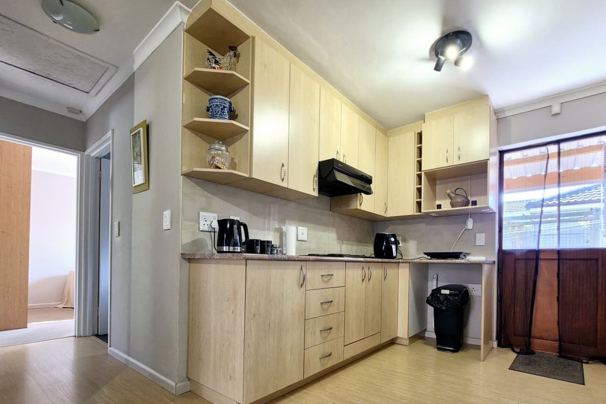 A functional kitchen featuring light wood-tone cabinetry, laminate countertops, and an integrated extractor fan, with direct access to an exterior door.