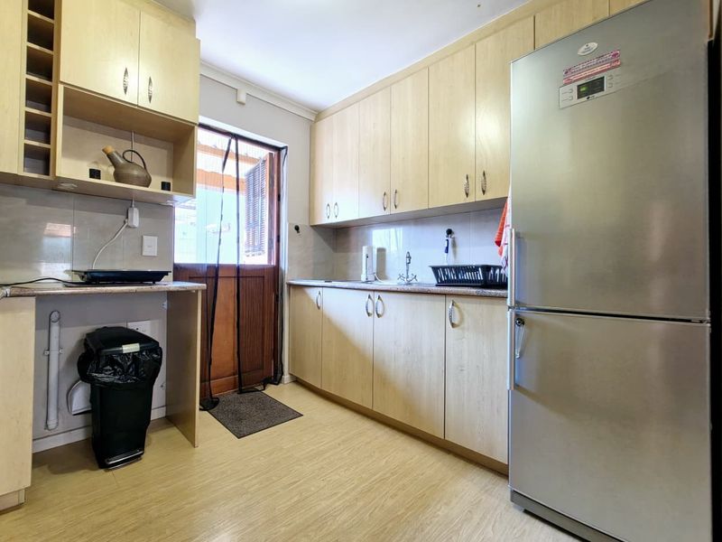 A functional kitchen featuring light wood-tone cabinetry, laminate countertops, a tiled backsplash, and direct access to an outdoor area.