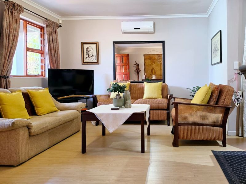 A comfortable living room featuring laminate flooring, a wall-mounted air conditioning unit, and natural light through a timber-framed window.