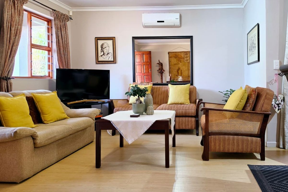 A comfortable living room featuring laminate flooring, a wall-mounted air conditioning unit, and natural light through a timber-framed window.