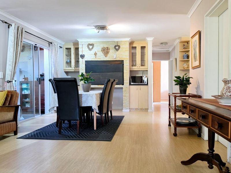 Open-plan living and dining area featuring light laminate flooring, a stone-clad feature wall with built-in cabinetry, and sliding glass doors leading to the patio.