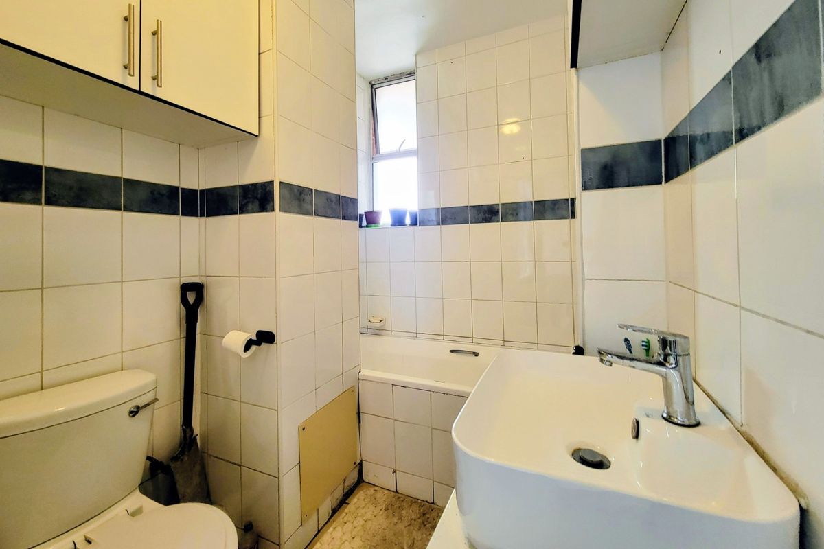 Compact bathroom featuring a white bathtub, wall-mounted vanity cabinet, and ceramic basin with chrome fixtures, requiring cosmetic updates to modernize the space.